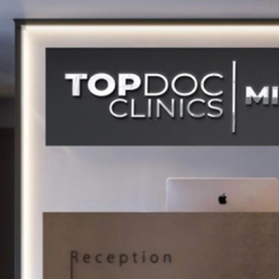 Top Doc Clinics Logo On The Wall Behind The Reception Desk In One Of Their Office Lobbies.