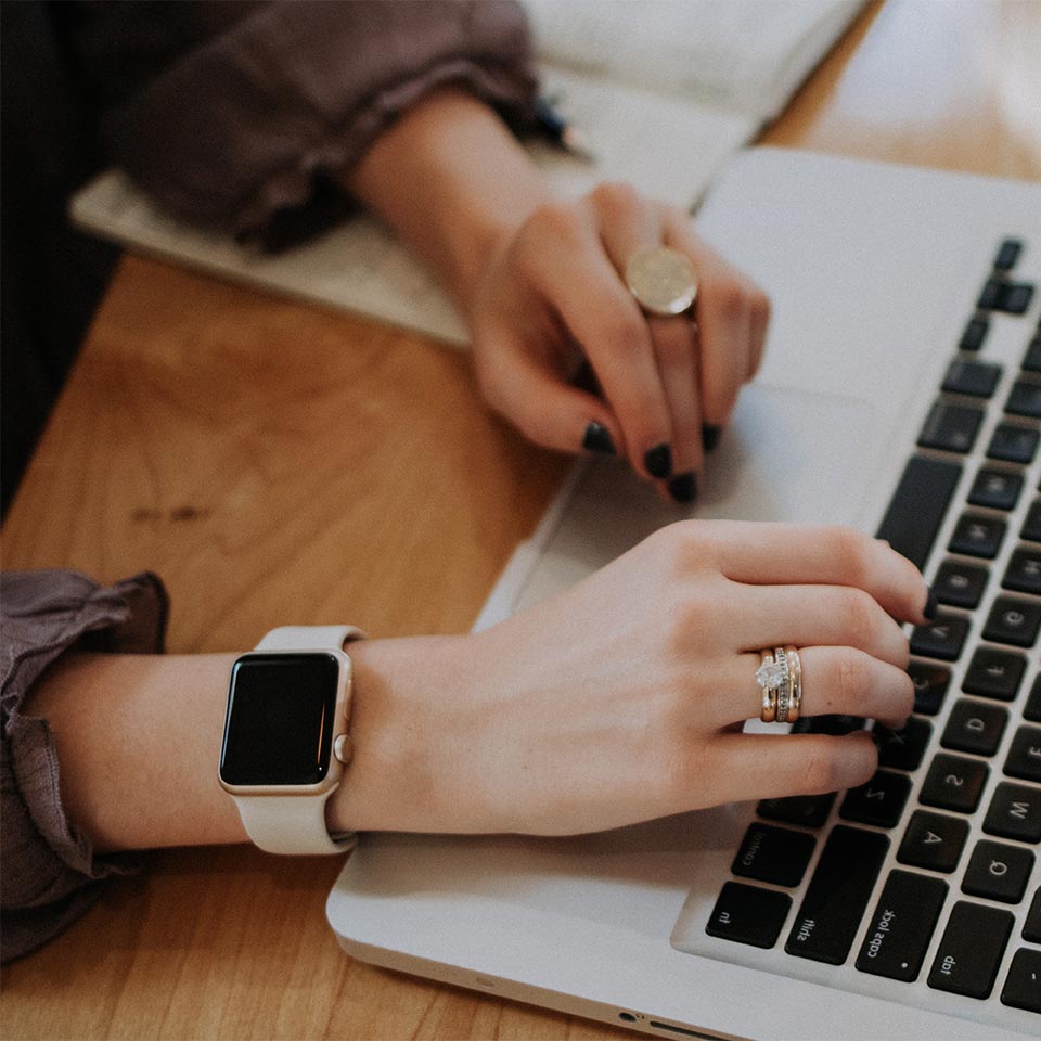 Close Up Of A Woman's Hands Wearing Jewelry And Typing On A Laptop Keyboard.